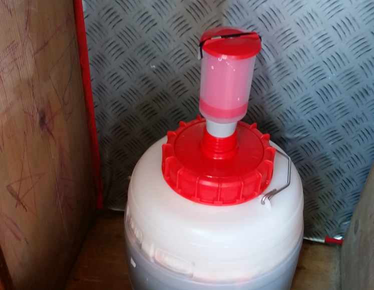 The carboy sitting in a cabinet. Notice the lower water level in the airlock.